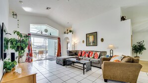 A spacious living room with a large window, a sofa set, a coffee table, and a wooden side table. - 4 Mi to Disney: Family Getaway w/ Game Room! (Kissimmee)