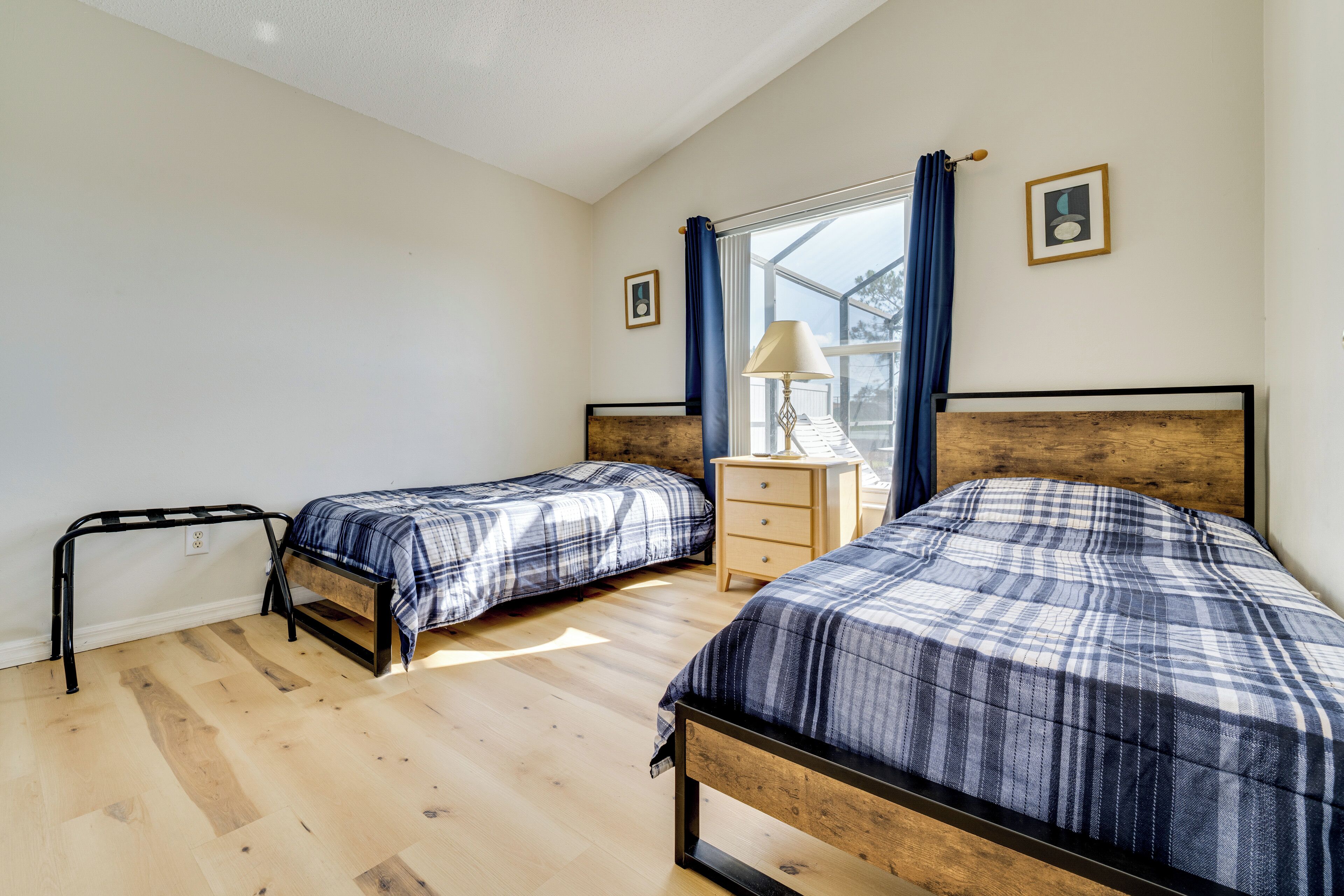 Een slaapkamer met twee bedden, een houten vloer, een nachtkastje en een raam met gordijnen.