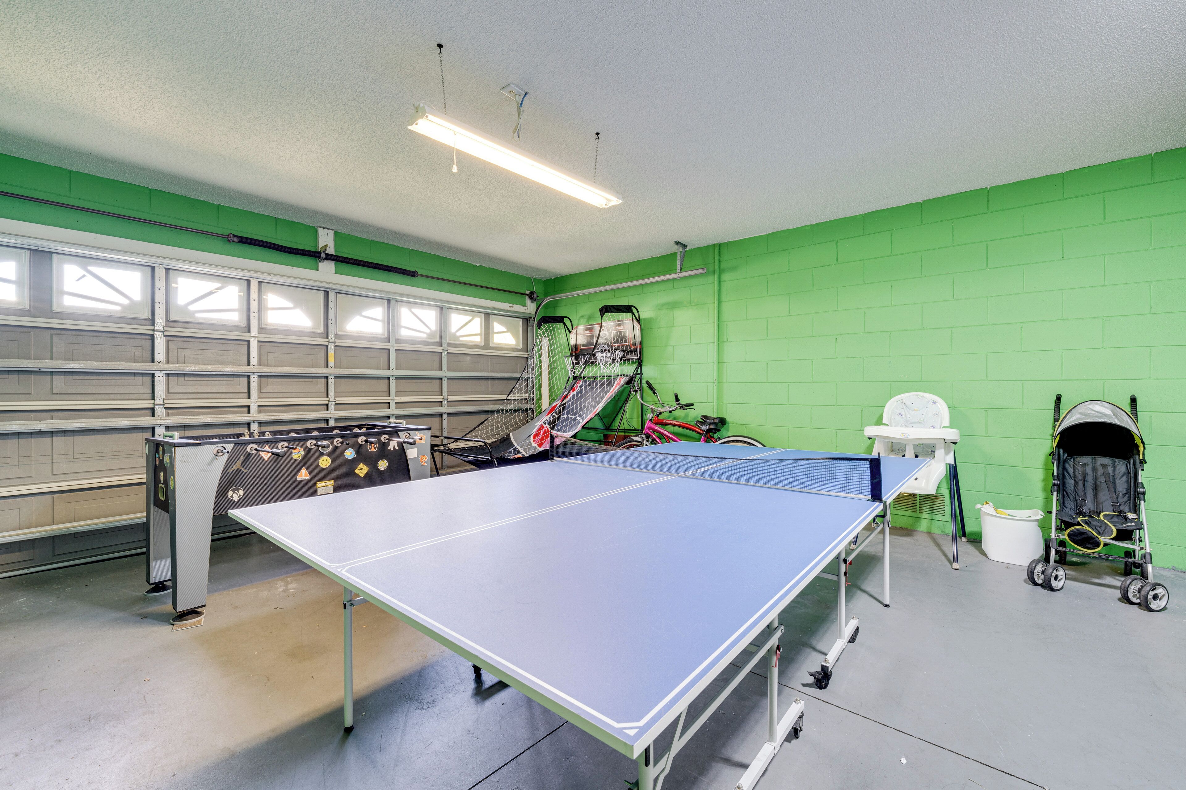 A ping pong table in a room with green walls, a bicycle, and a stroller.
