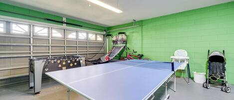 A ping pong table in a room with green walls, a bicycle, and a stroller.