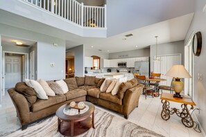 A spacious living area with a brown sectional sofa, a round coffee table, and a dining table with chairs. A kitchen is visible in the background with white cabinets and a microwave. - Luxe Davenport Home: Private Pool, Resort Perks! (Davenport)