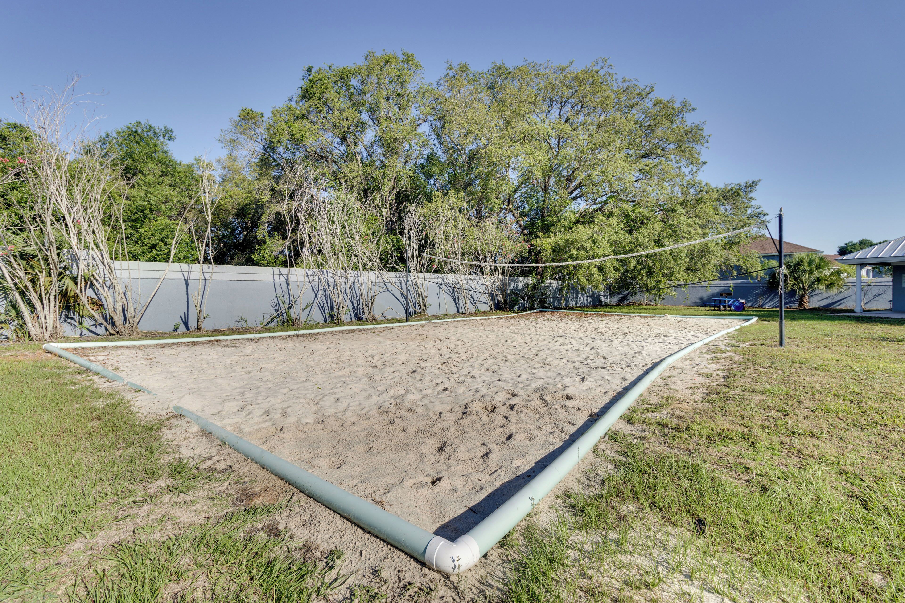 A volleyball court with a net, surrounded by trees and a building in the background.