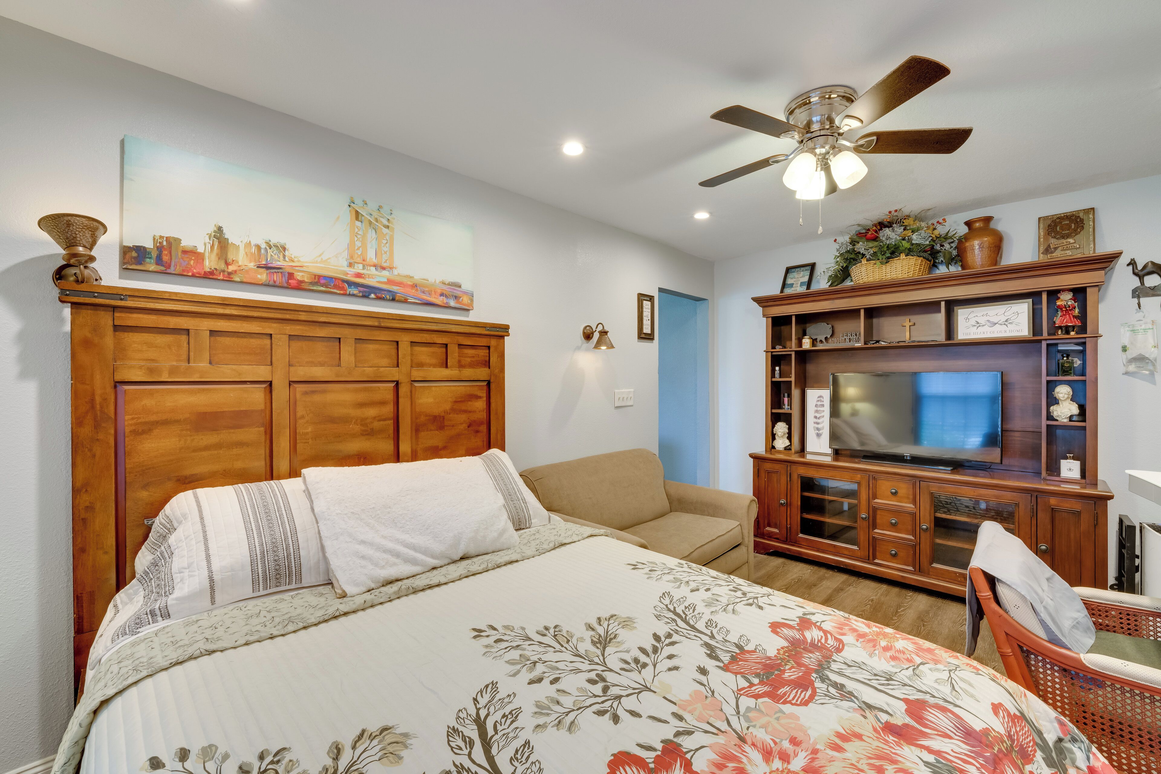 Une chambre à coucher comprenant un lit, une tête de lit en bois, un téléviseur, une armoire en bois et un ventilateur de plafond.