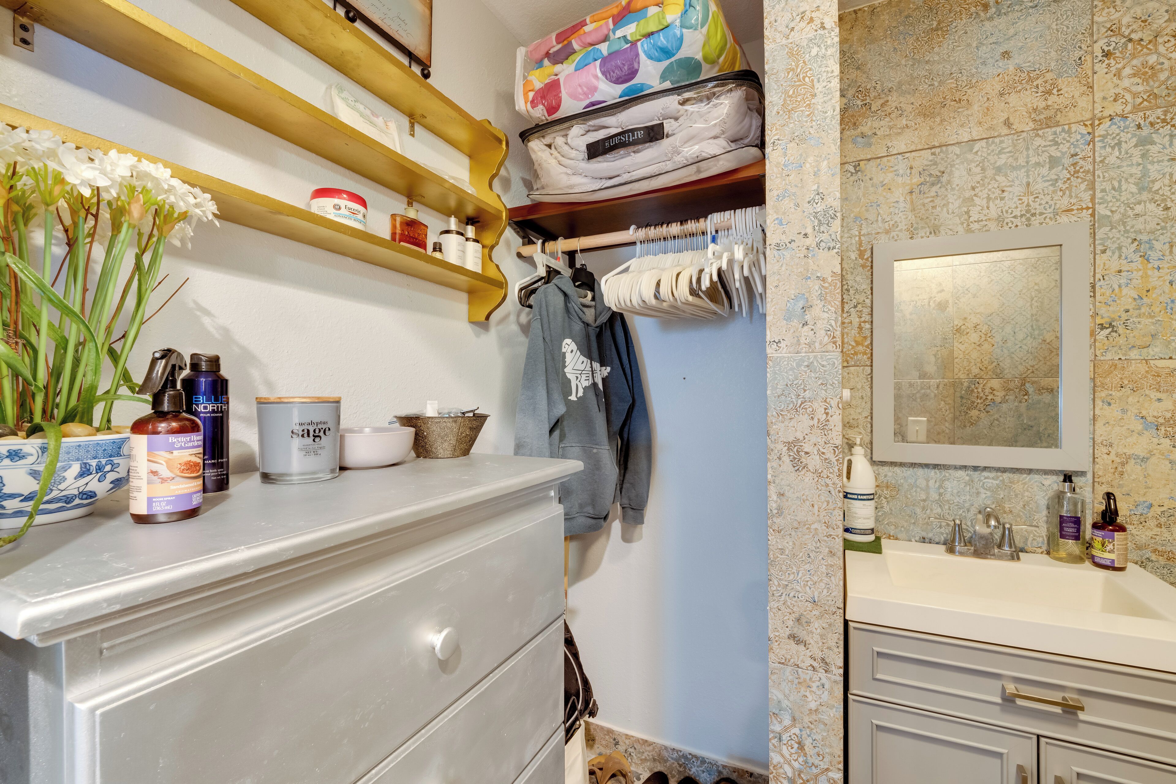 Une salle de bain équipée d’un lavabo, d’un miroir et d’étagères où sont rangés les produits de toilette.