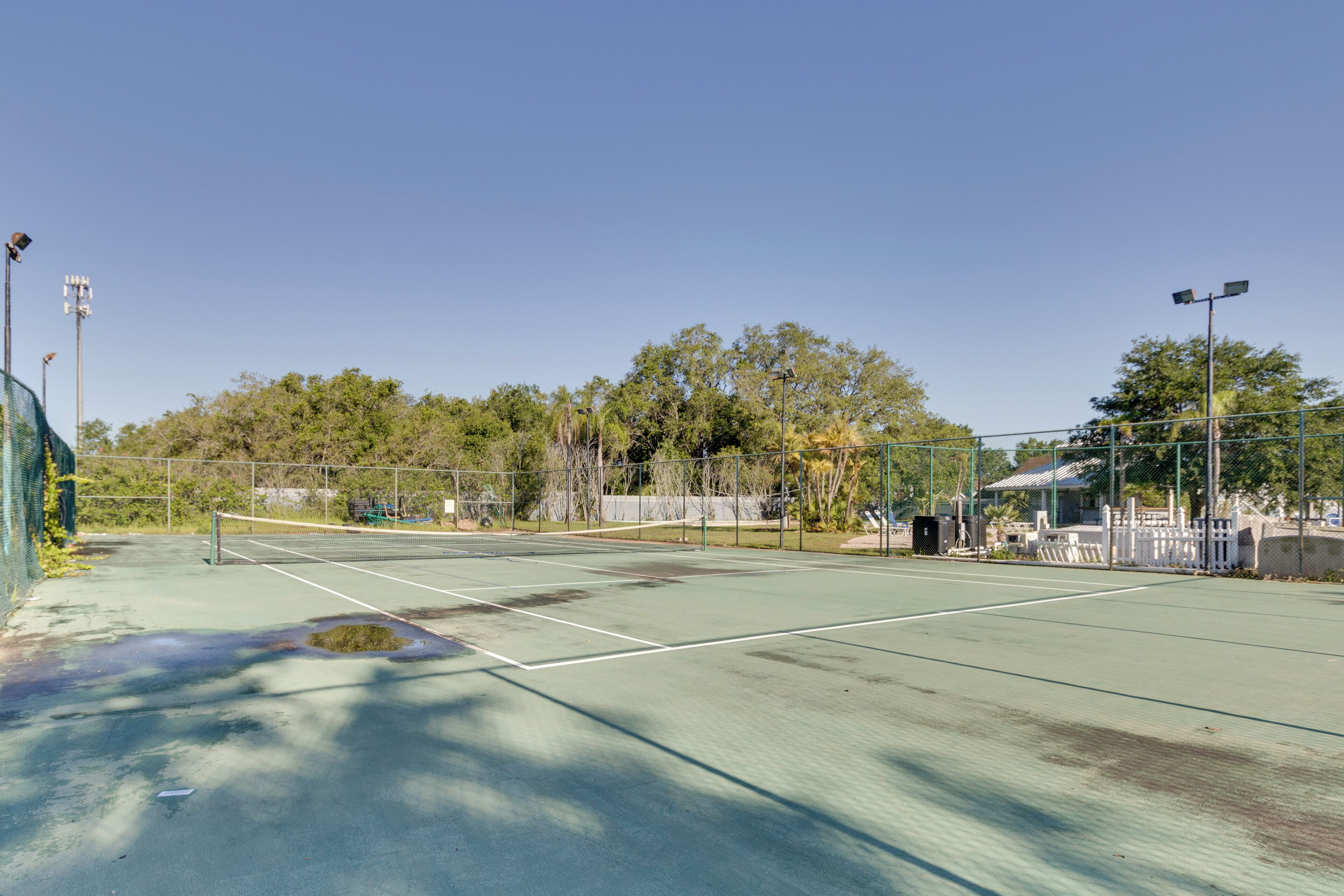 An outdoor tennis court with a net, surrounded by trees and a fence.