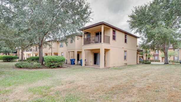 A two-story building with a balcony, surrounded by trees and a grassy lawn. - 9 Mi to Disney: Davenport Townhome w/ Patio (Davenport)