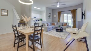 A modern living room with a dining area, a kitchen in the background, and a white chair with a tray. - 9 Mi to Disney: Regal Palms Townhome w/ Patio! (Davenport)