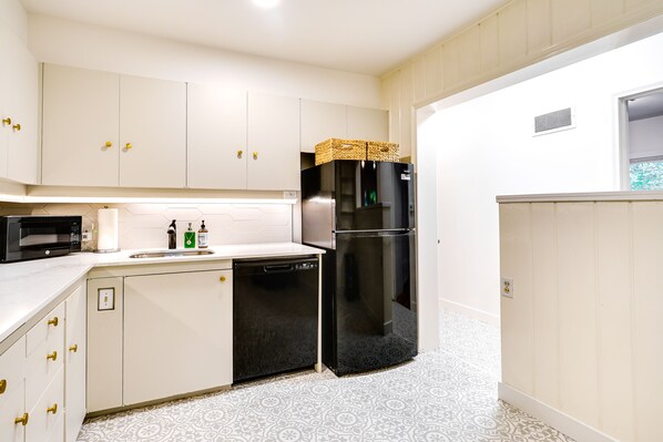 Une cuisine de taille réduite avec des meubles blancs, un réfrigérateur noir, un four à micro-ondes et un lave-vaisselle.
