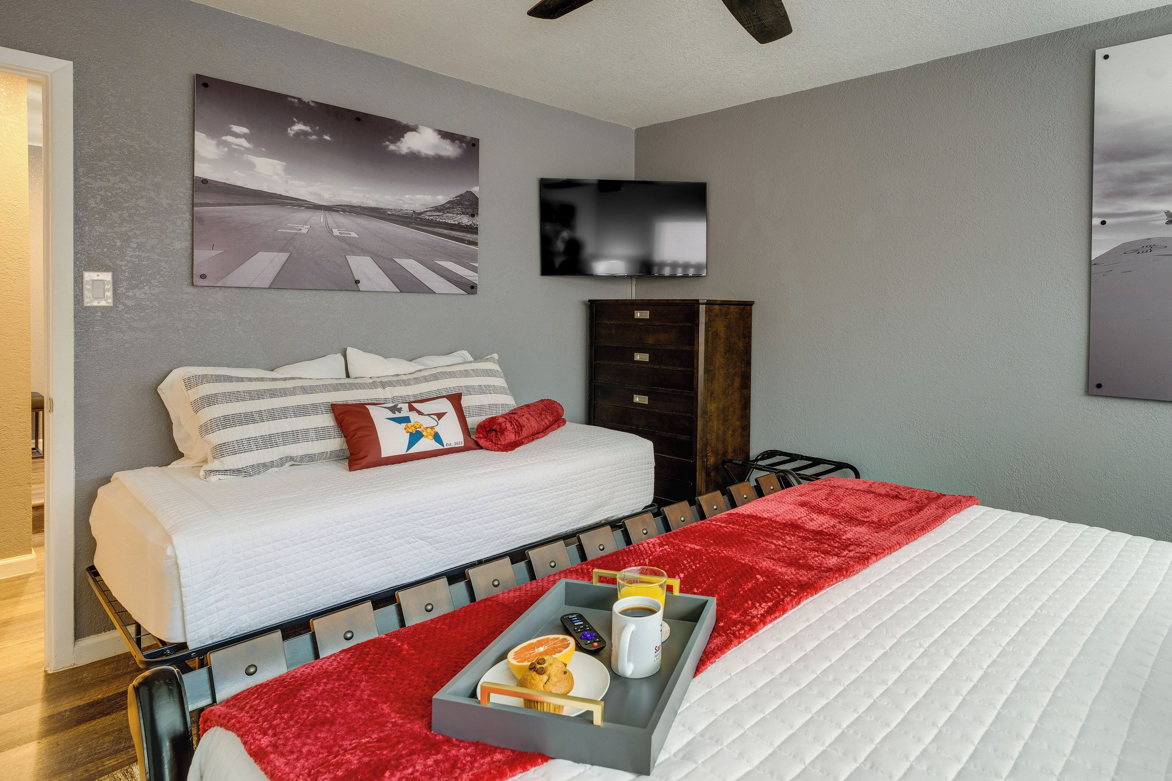 A hotel room with a bed, a tray with breakfast items, a flat-screen TV, and artwork on the walls.