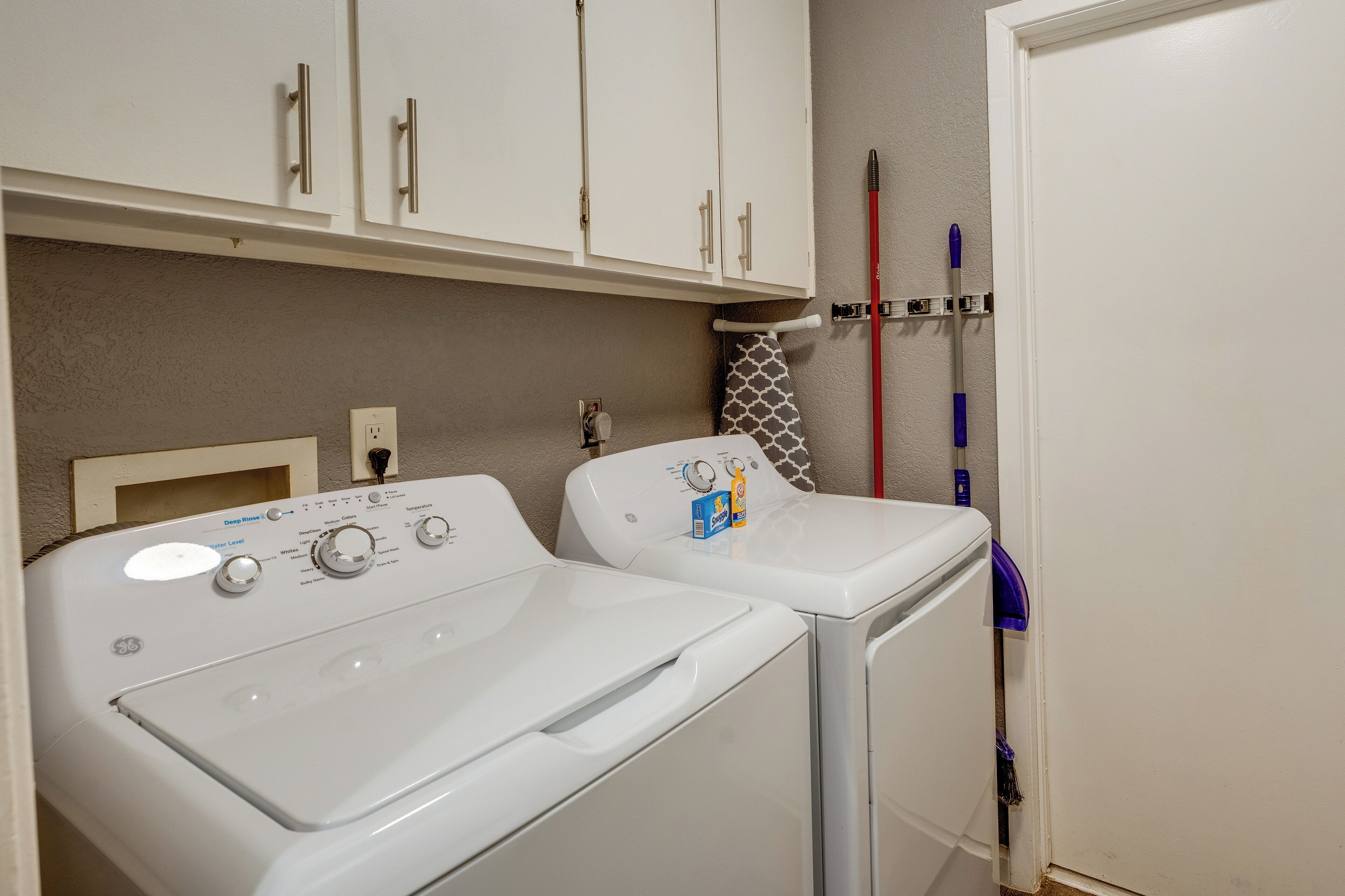 A laundry area with two front-loading washing machines, a wall-mounted drying rack, and a door with a towel hanging on it.