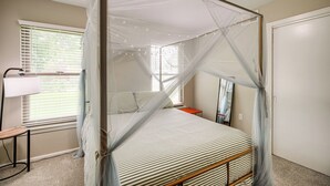 Une chambre à coucher avec un lit à baldaquin, une table de chevet, une lampe et une fenêtre avec des stores.