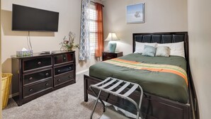 A bedroom with a bed, a dresser, a TV, a lamp, and a window with curtains.