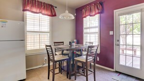 A kitchen with a dining table, chairs, a refrigerator, and a window with blinds.