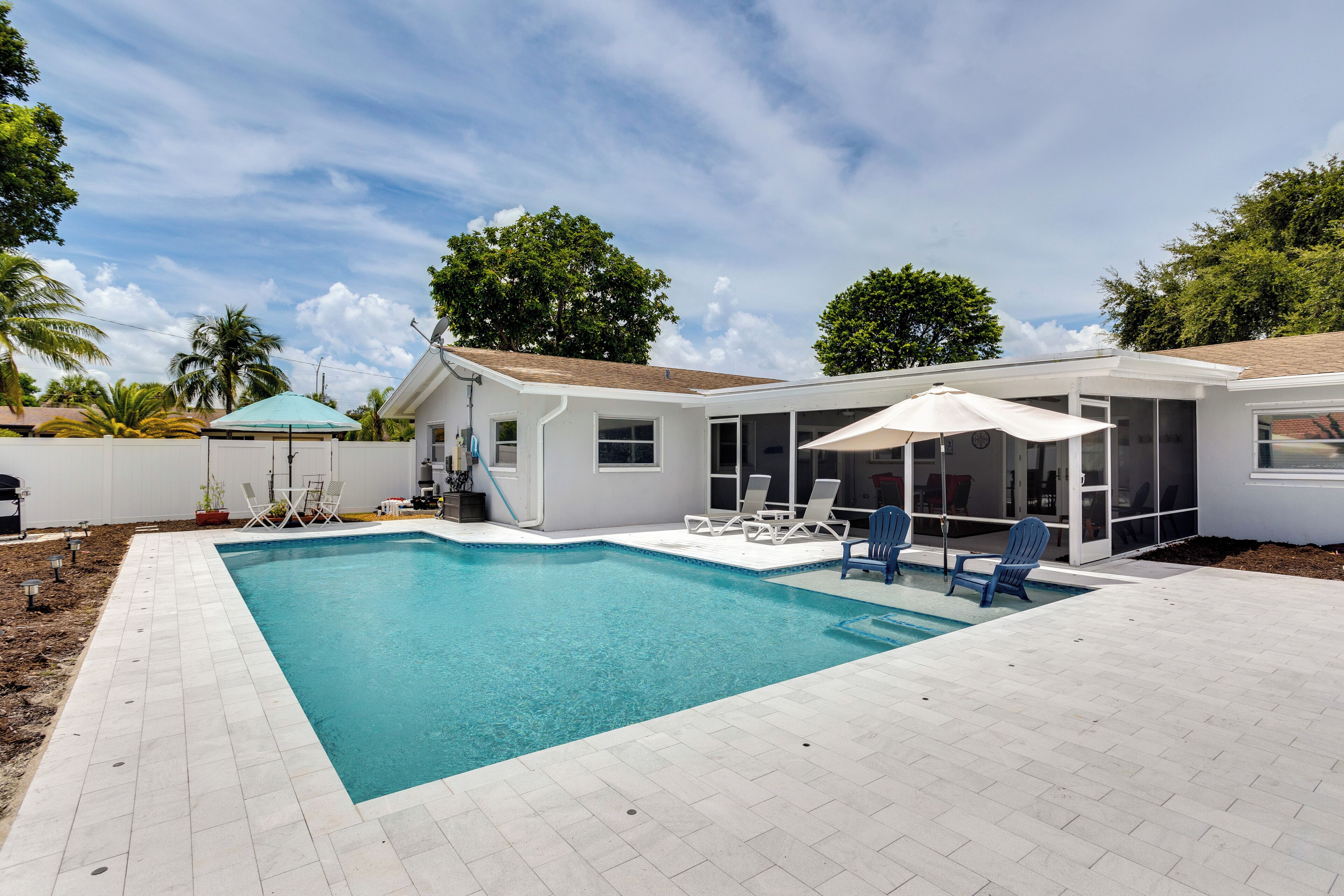 A rectangular swimming pool with a tiled deck, surrounded by lounge chairs and umbrellas.