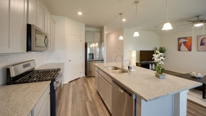 A modern kitchen with stainless steel appliances, a central island with a sink, pendant lighting, and a view into the dining area. - San Antonio Getaway w/ Private Yard & Smart TV (San Antonio)