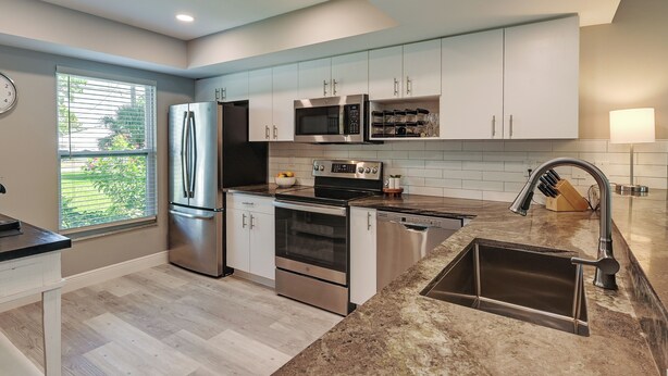 A modern kitchen with stainless steel appliances, white cabinetry, and a large window.