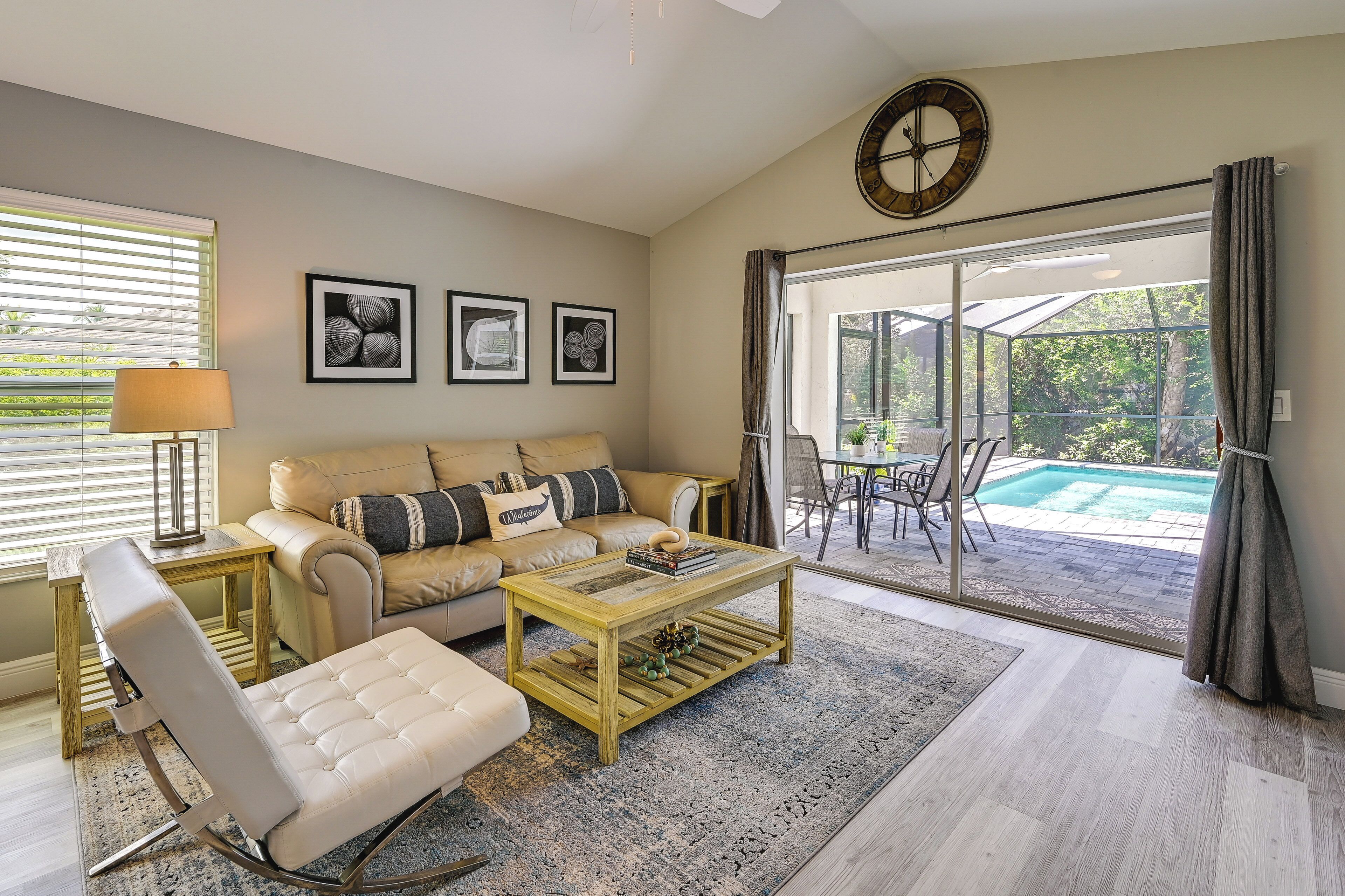 A living room with a sofa, coffee table, and a chair, a dining area with a table and chairs, and a view of a pool through large glass doors.