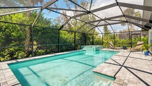 A clear swimming pool with a glass enclosure, surrounded by a patio area with chairs and a potted plant.