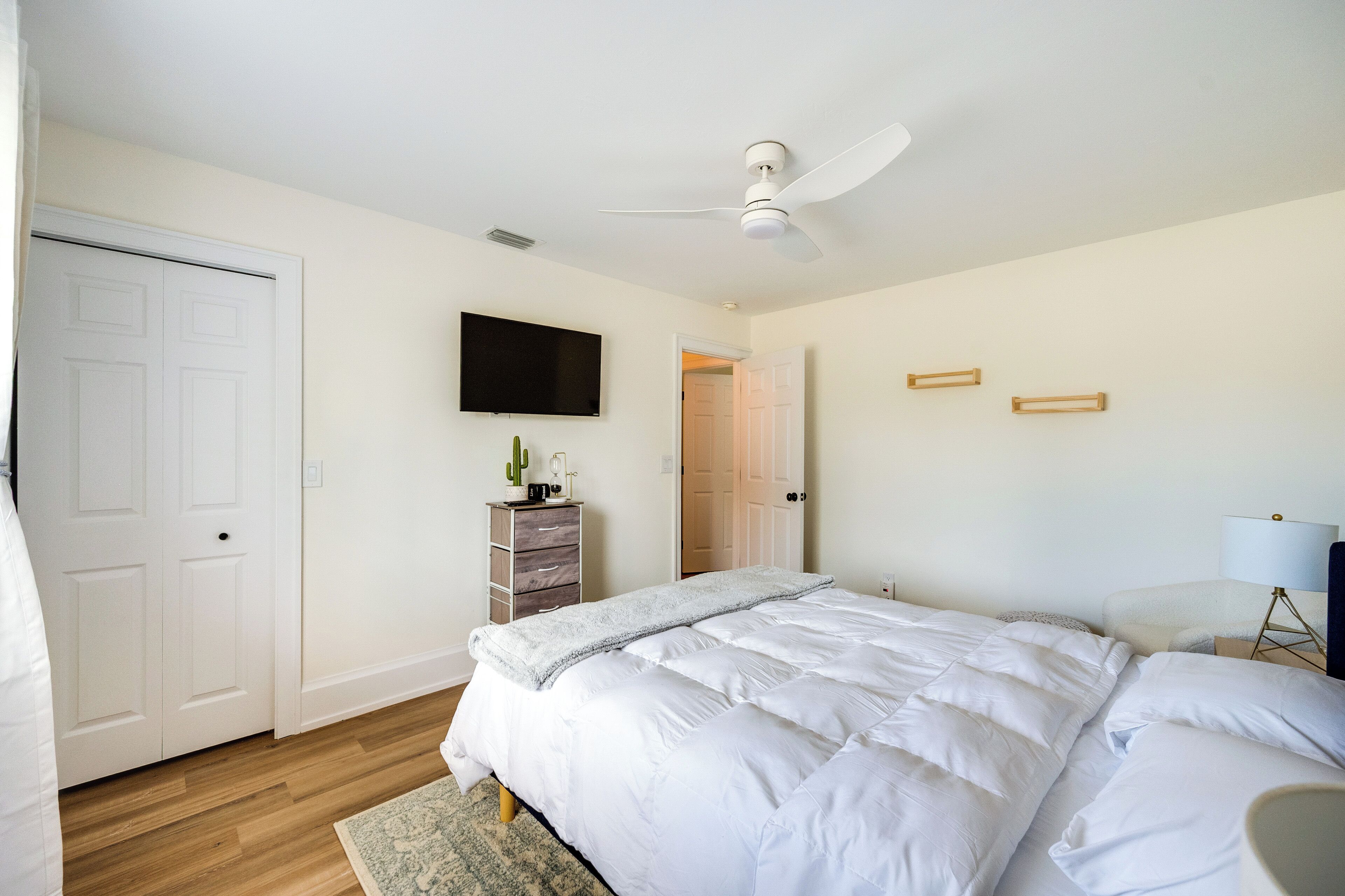 A bedroom with a bed, a ceiling fan, a TV, a dresser, and a door.