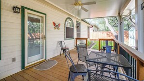 A covered porch with a ceiling fan, a table and chairs, a door with a green frame, and a butterfly decoration on the wall. - North San Antonio Vacation Rental w/ Yard & Deck! (San Antonio)