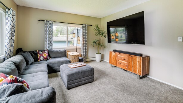 A modern living room with a sectional sofa, a flat-screen TV, a wooden cabinet, and a potted plant. - Anchorage Home ~ 7 Mi to Chugach State Park! (Anchorage)