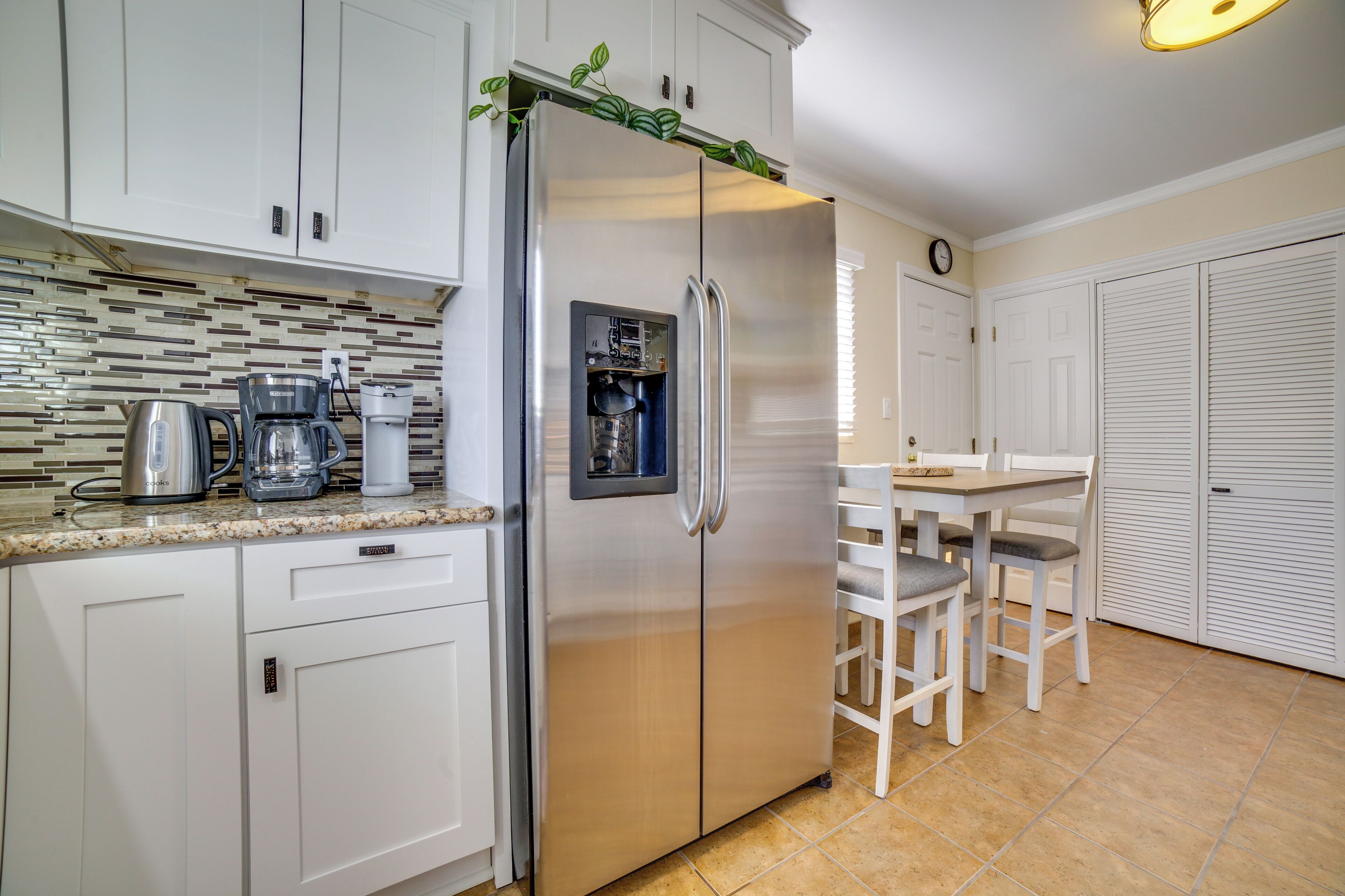 A modern kitchen with white cabinets, a stainless steel refrigerator, a coffee maker, and a water dispenser.