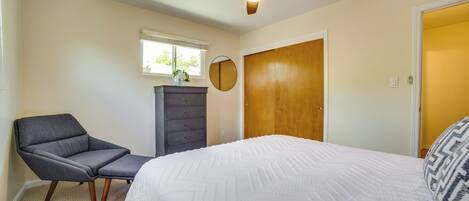 A bedroom with a bed, a chair, a dresser, a ceiling fan, a window, and a door.