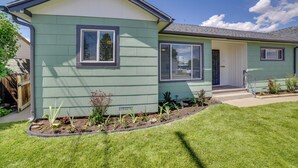 Een gelijkvloers huis met een veranda, een kleine tuin vol planten, en een helderblauwe lucht.