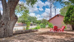 A backyard with a large tree, a red building, and a fence.