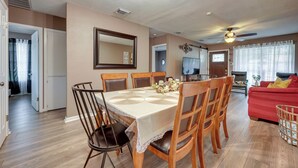 A dining area with a table set for four, a red sofa, and a ceiling fan in a living room.