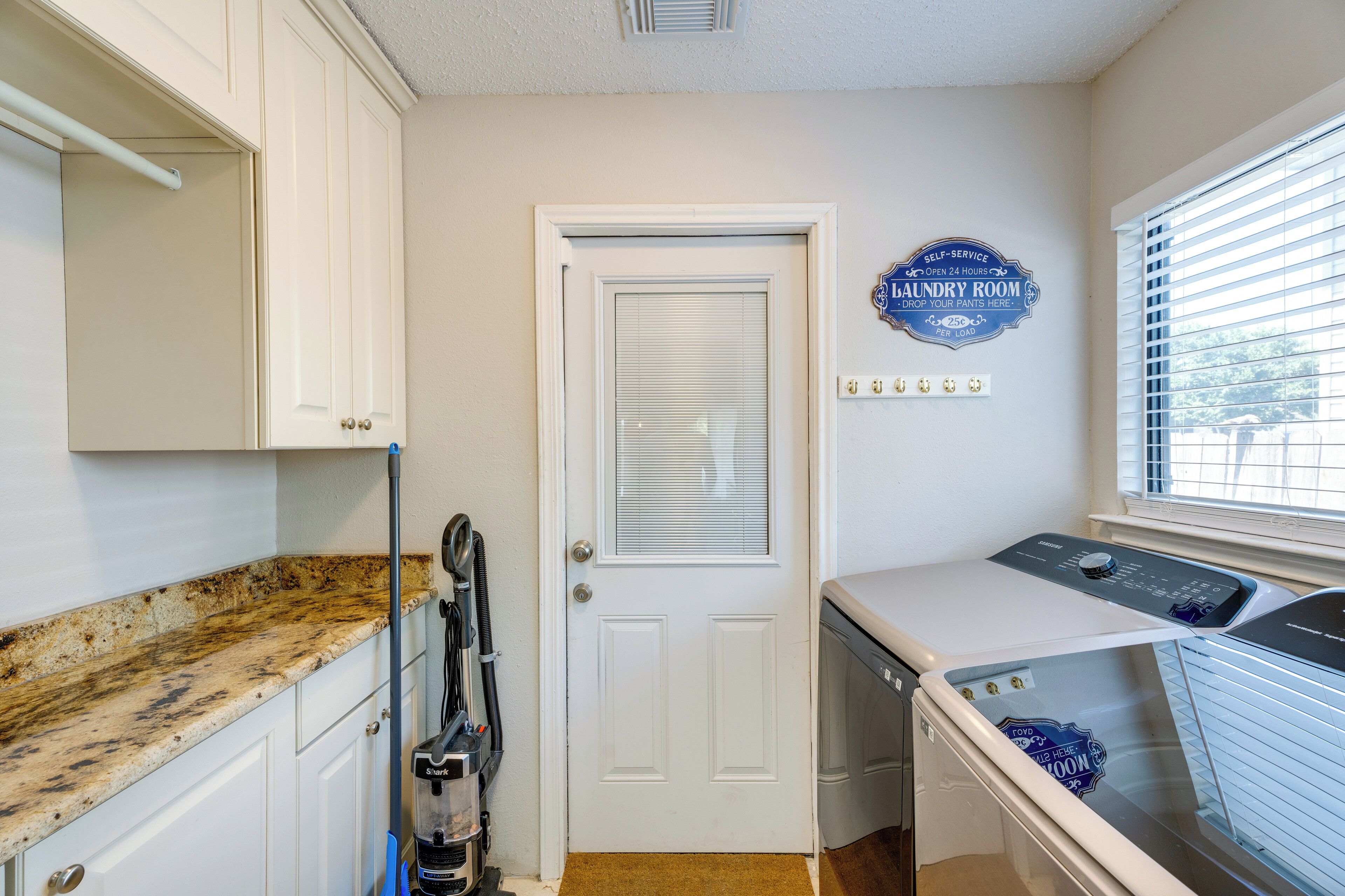 A laundry room with a door, a wall-mounted sign, a window with blinds, and a countertop.
