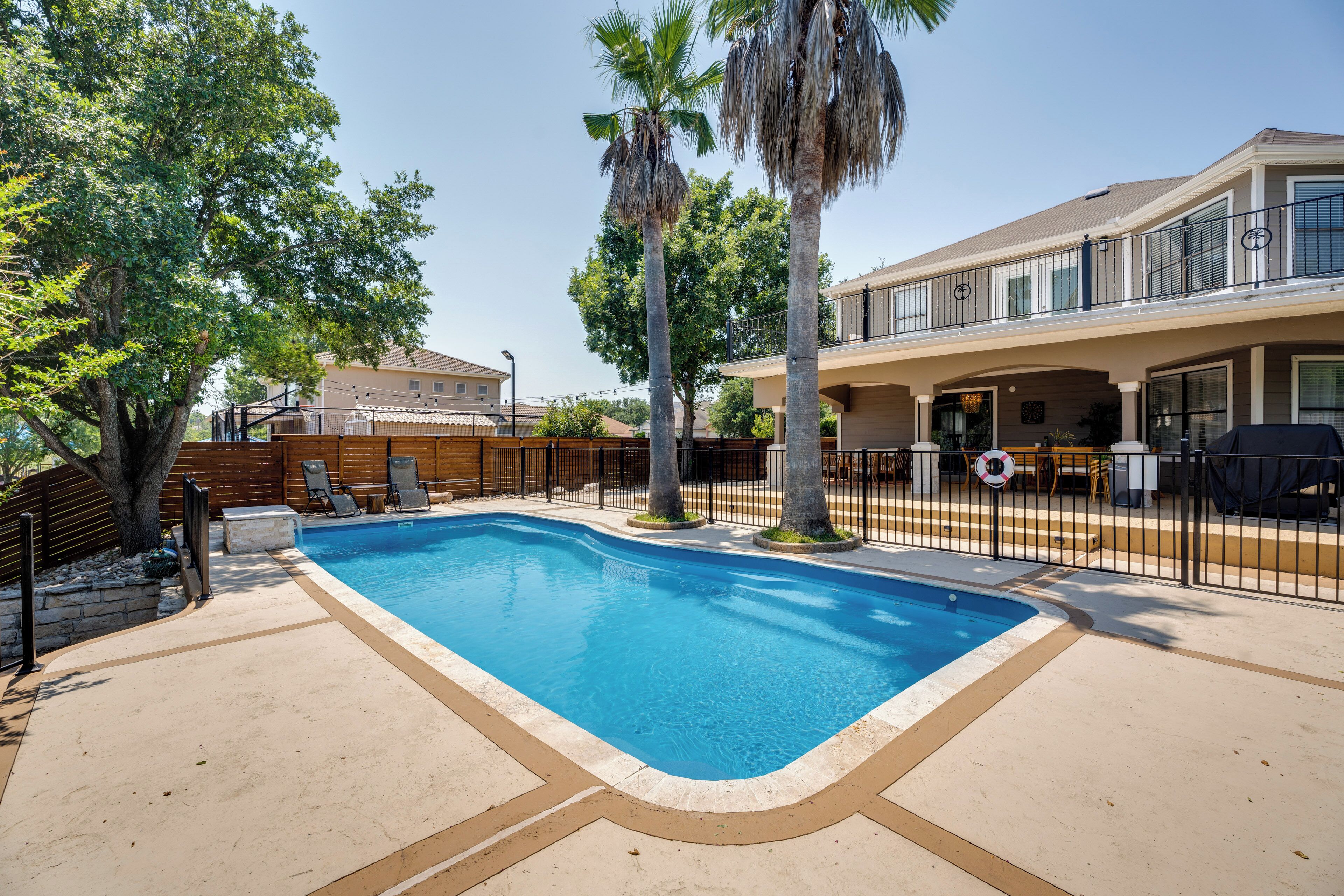 A swimming pool with a wooden deck, palm trees, and a fenced patio area.