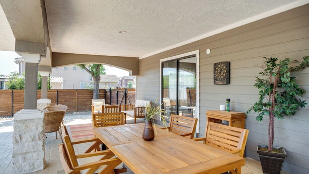 Une terrasse extérieure avec une table et des chaises en bois, une plante en pot et une porte-fenêtre coulissante donnant sur un balcon.