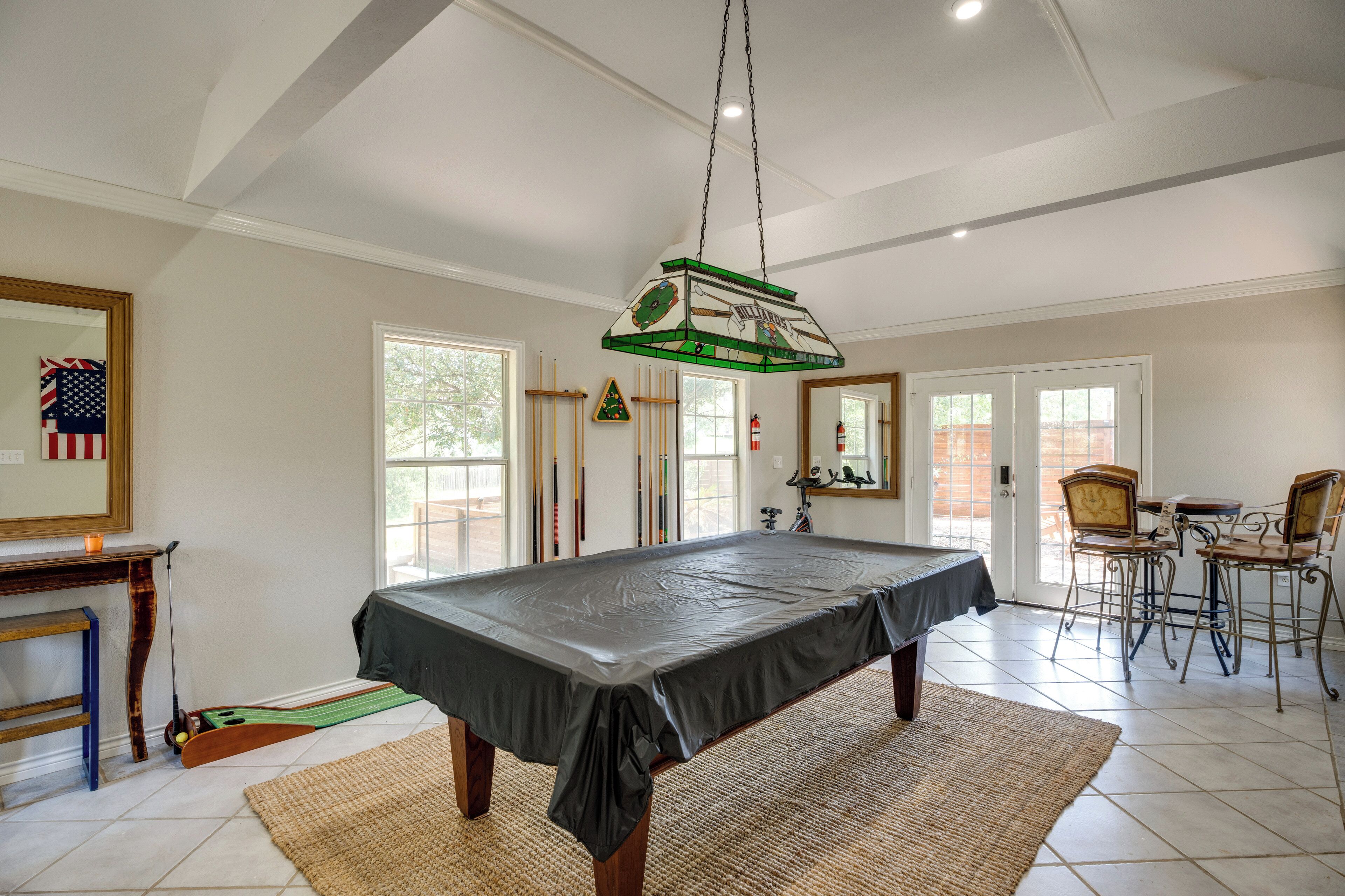 A pool table in a room with a high ceiling, a fireplace, and a dining area with chairs.