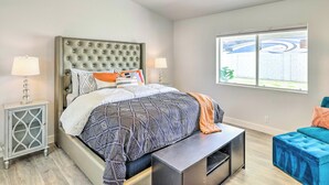 A bedroom with a large bed, bedside tables, a bench, a window, and a view of the outside.