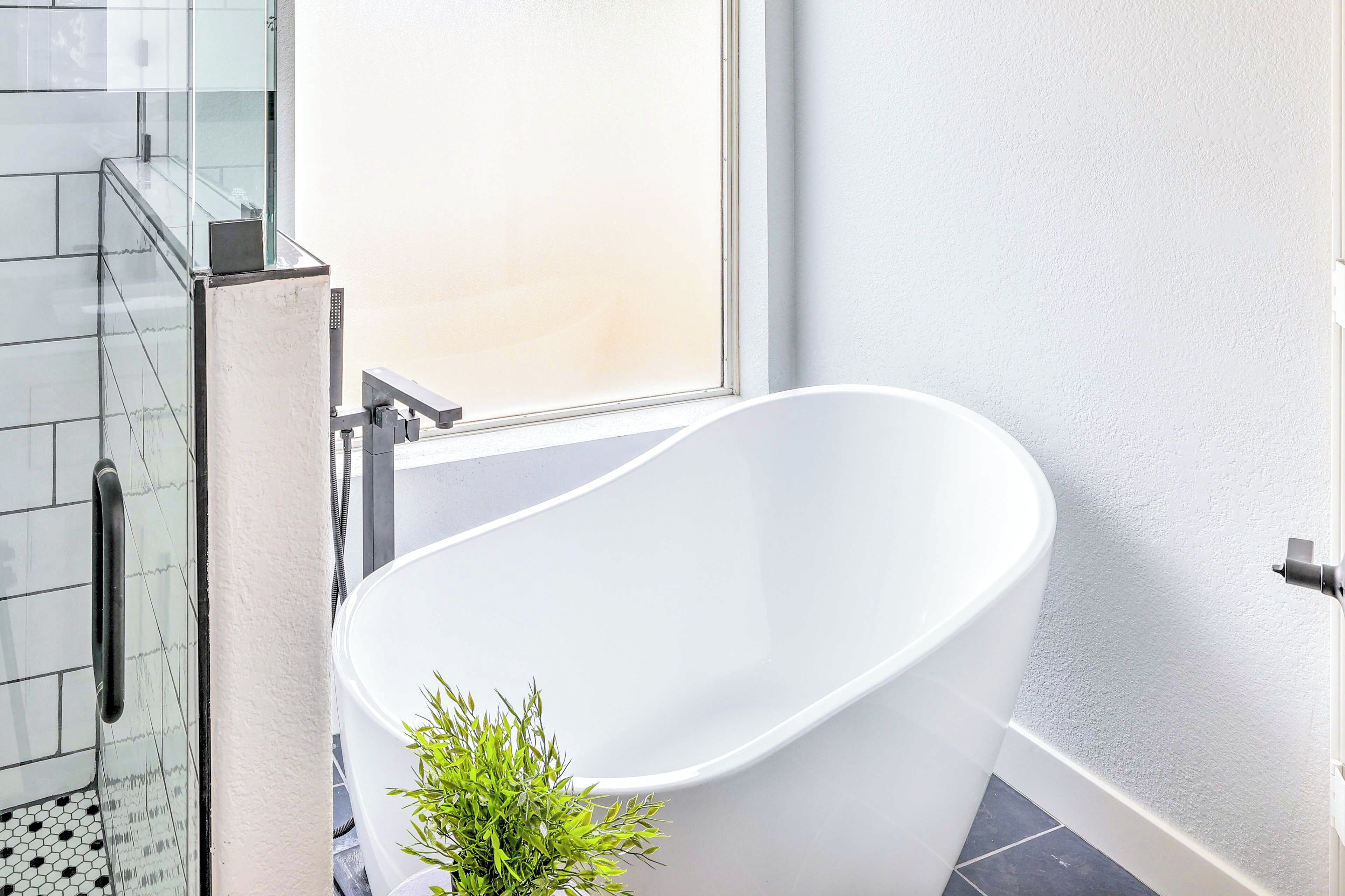 A modern bathroom with a freestanding bathtub, a glass shower enclosure, and a small potted plant.