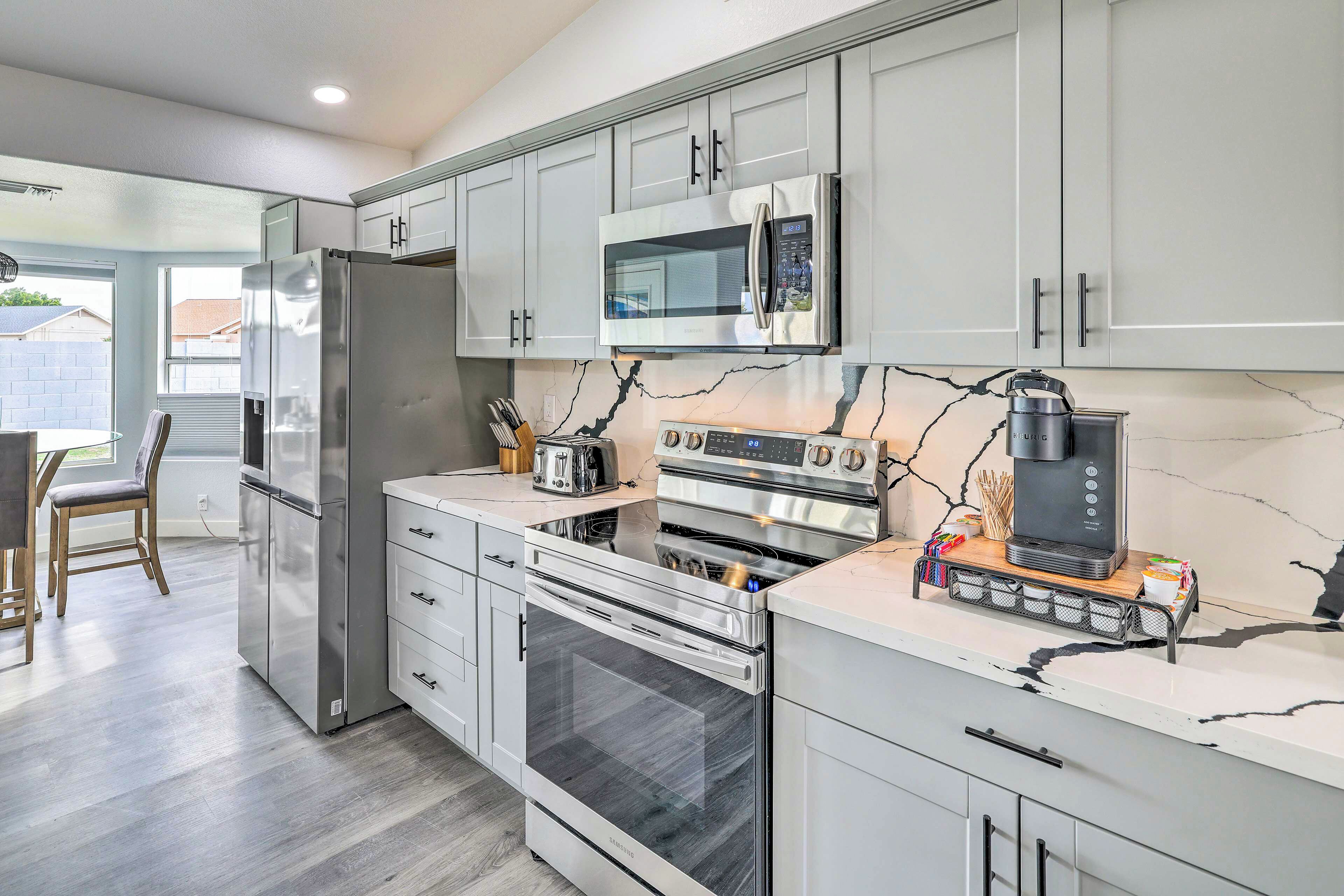 A modern kitchen with stainless steel appliances, white cabinetry, and a marble backsplash.
