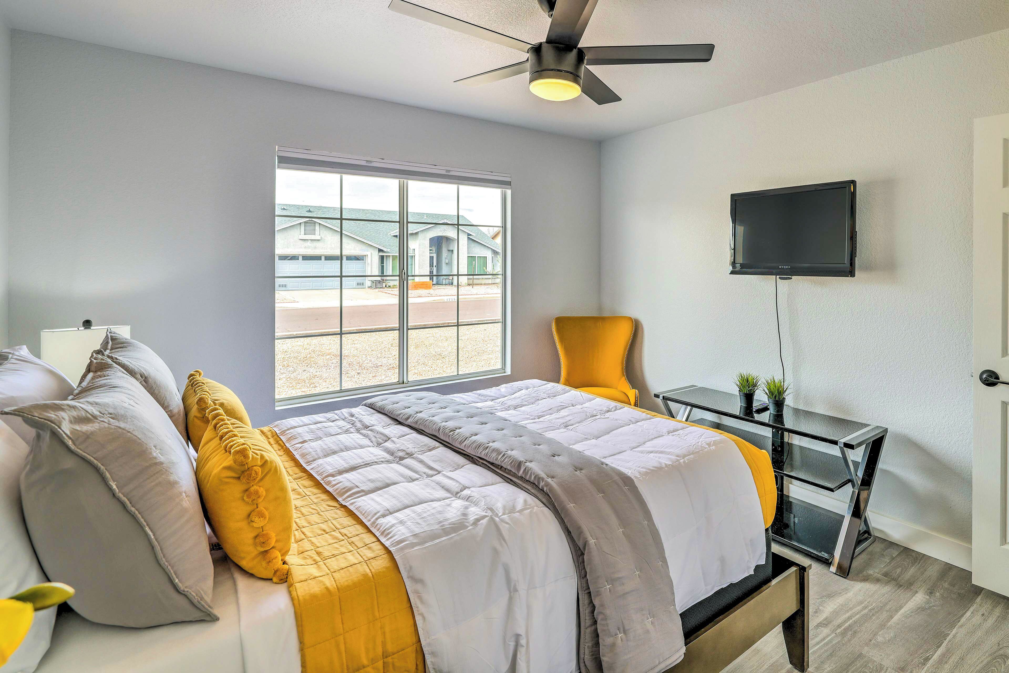 A bedroom with a bed, a desk, a chair, a TV, and a window with a view of buildings.