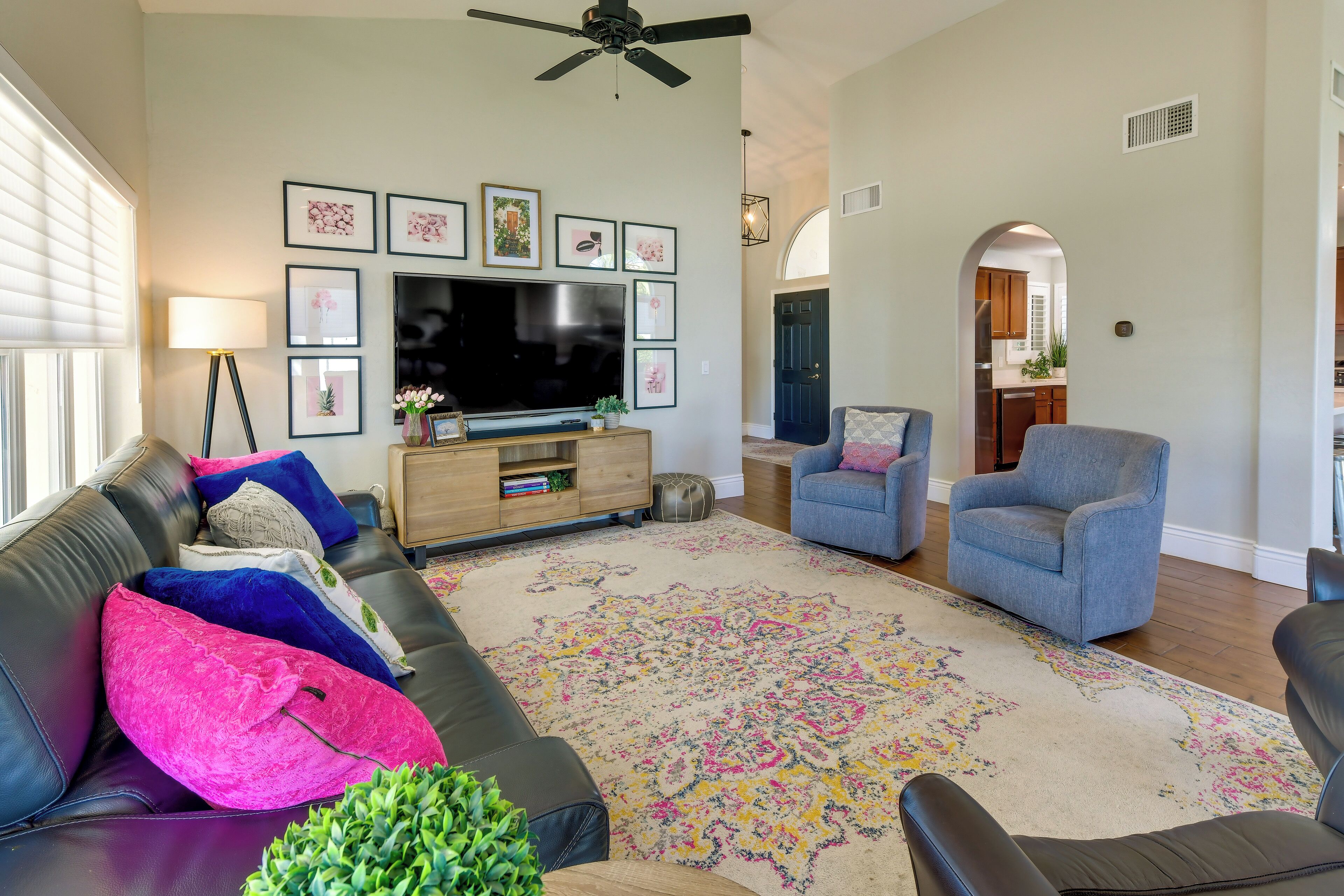 A living room with a black leather sofa, a blue armchair, a large TV, and a patterned rug.