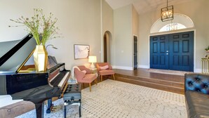 A grand piano, two pink armchairs, a white rug, and a blue door in a spacious living area. - 1 Mi to Water Ranch! Family Retreat w/ Resort Pool (Gilbert)