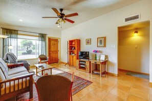 A living room with a sofa, chairs, a TV stand, and a ceiling fan.