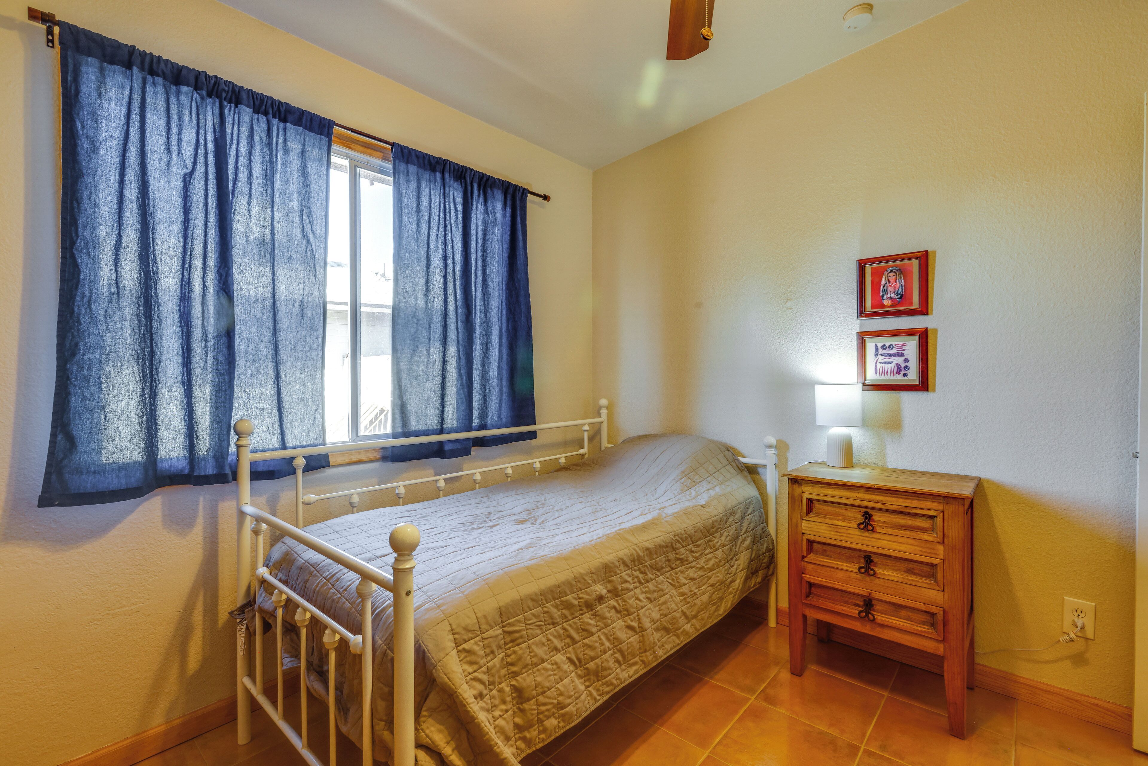 Un dormitorio con una cama individual, una mesita de noche, una lámpara y una ventana con cortinas.