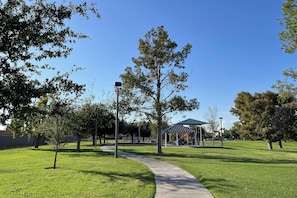 A park with a paved walkway, trees, and a covered play area.