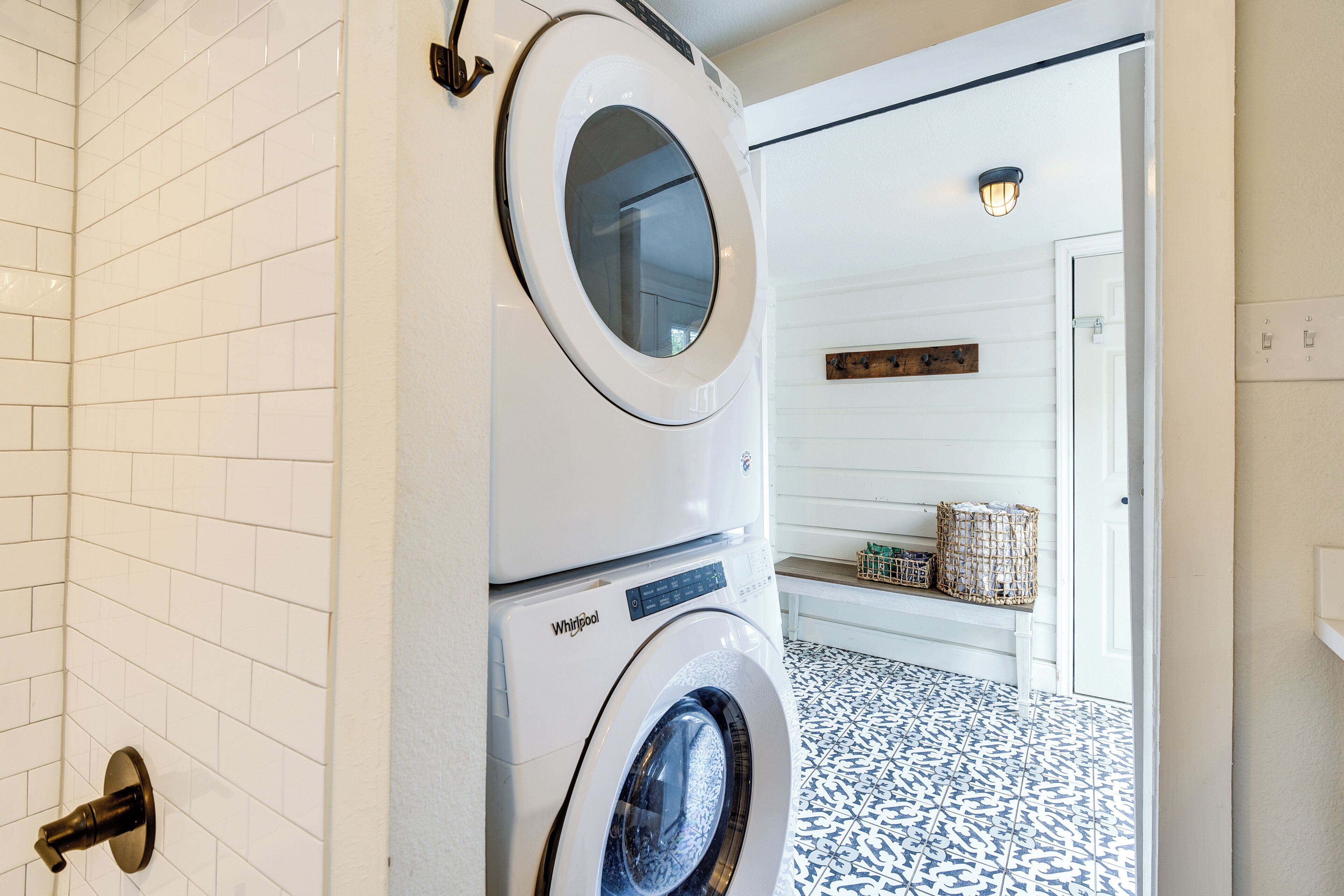 A laundry room with stacked washers and dryers, white tiled walls, and a patterned floor.