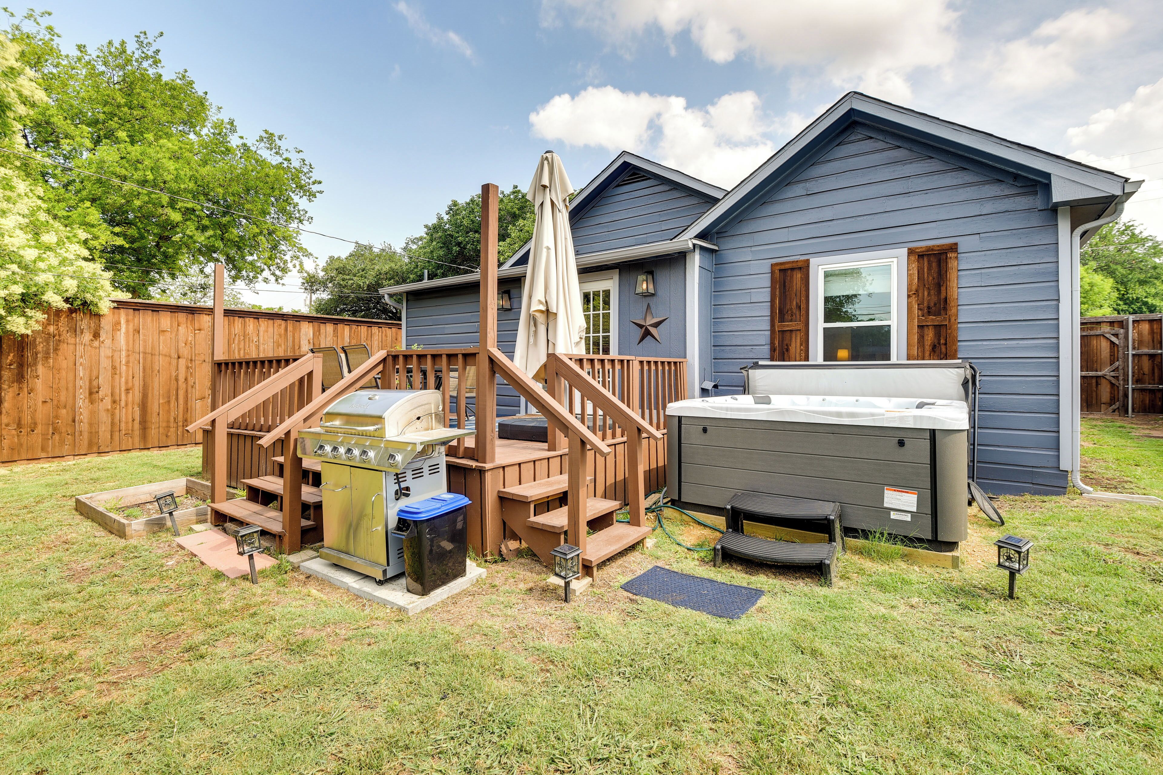 A backyard with a wooden deck, hot tub, grill, and a house with a blue exterior.