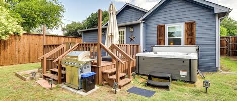 A backyard with a wooden deck, hot tub, grill, and a house with a blue exterior.
