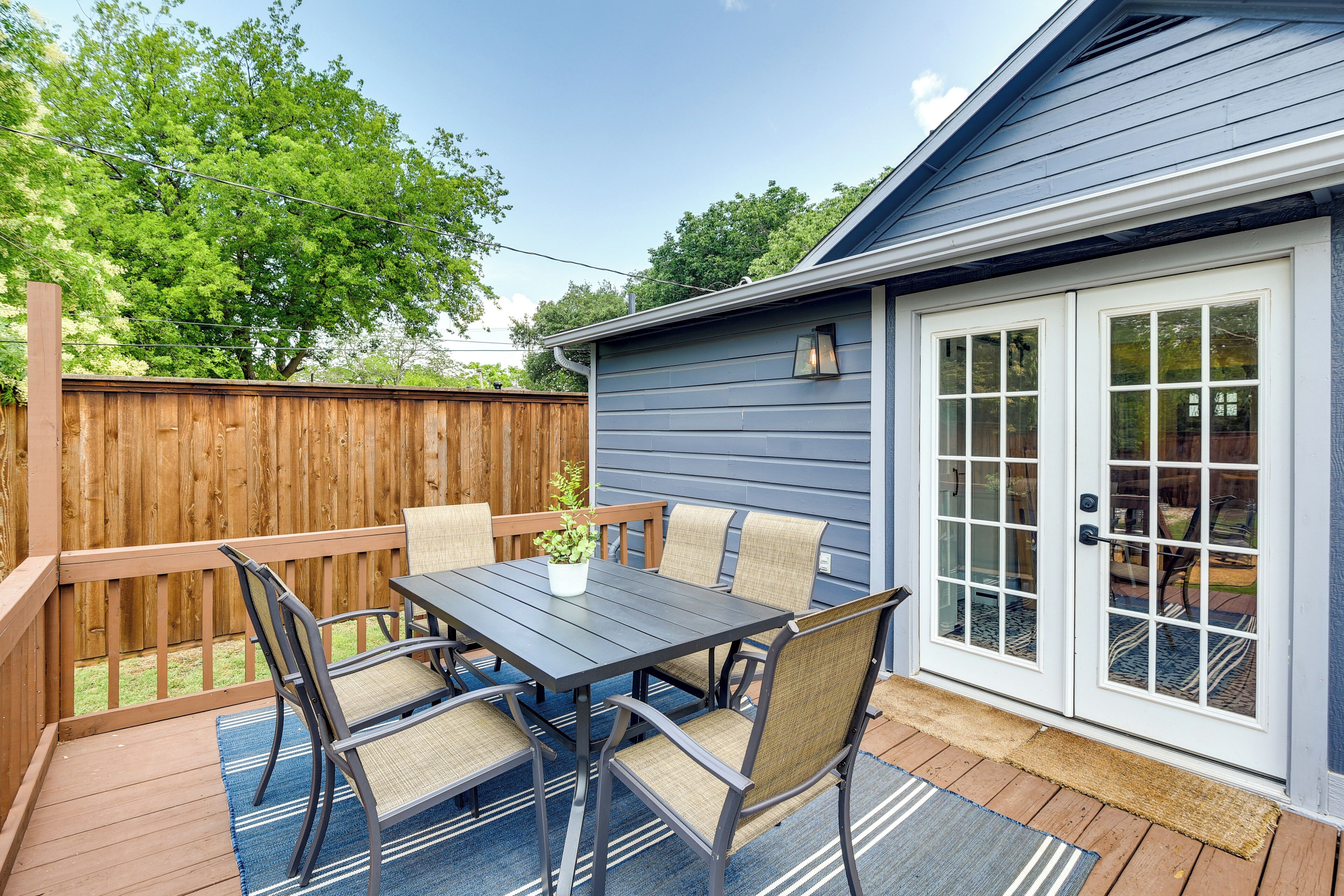 A deck with a table and chairs, a wooden fence, and a house with a blue exterior and a glass door.