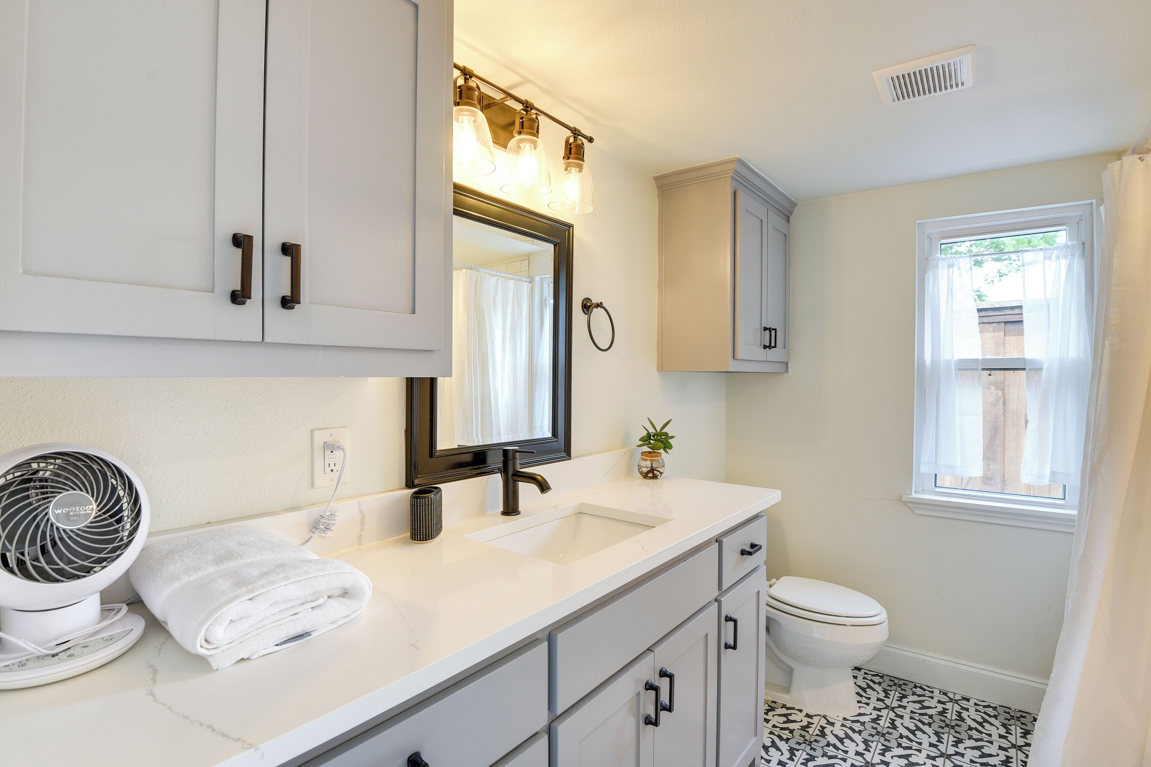 A bathroom with a white vanity, a sink, a mirror, a fan, and a toilet.