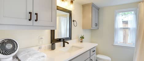 A bathroom with a white vanity, a sink, a mirror, a fan, and a toilet.
