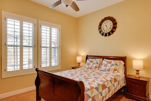 A bedroom with a wooden bed, two bedside tables with lamps, a wall clock, and a window with blinds. - Stunning Phoenix Vacation Rental w/ Private Pool! (Phoenix)